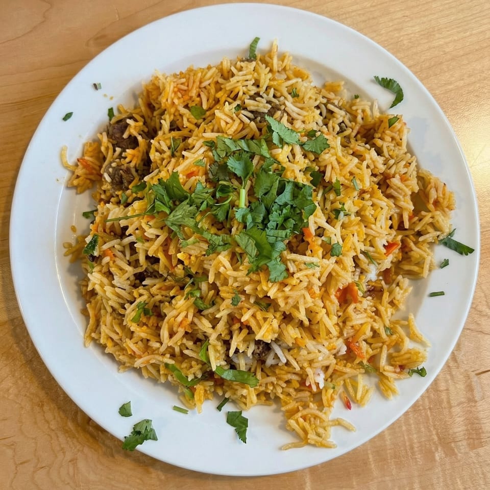 A white plate filled with golden biryani rice, garnished with fresh green cilantro.