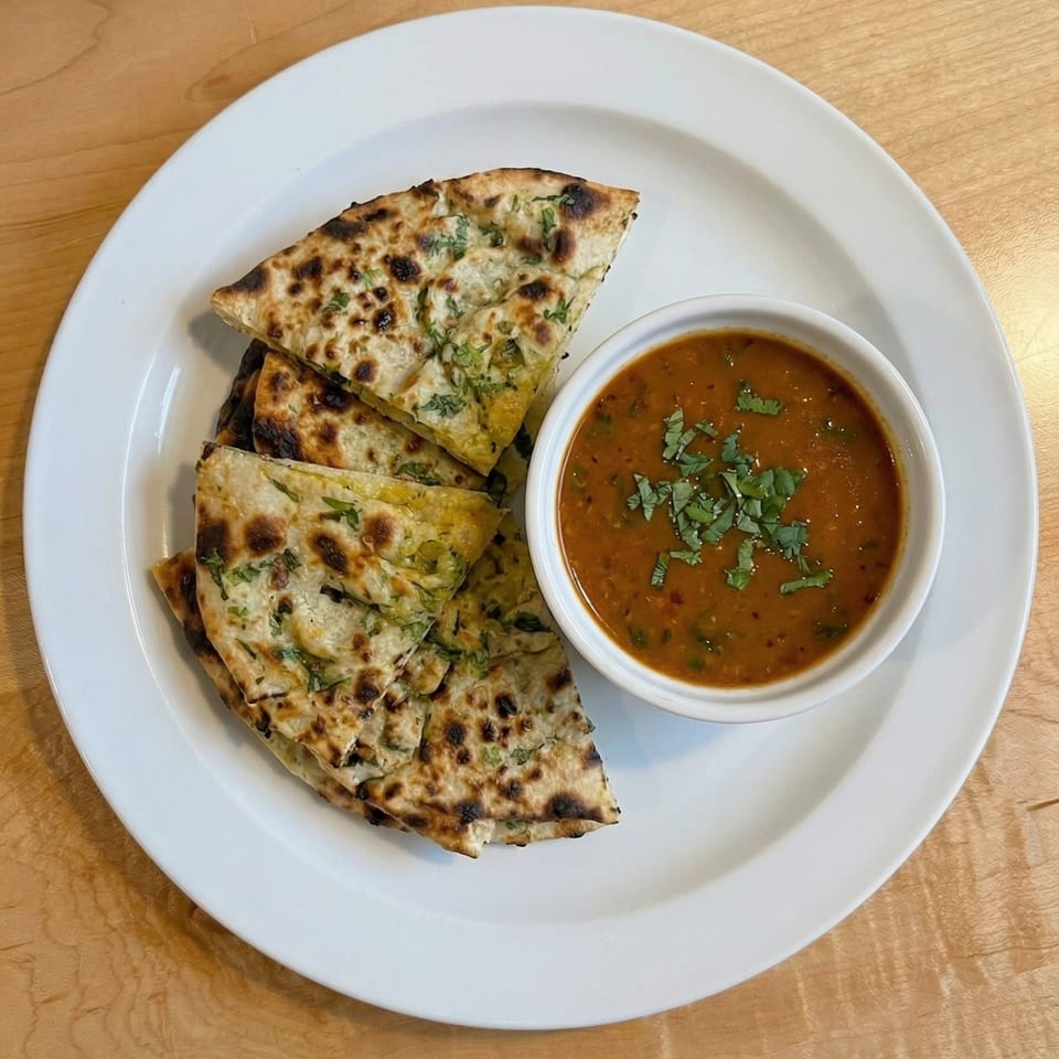 Naan bread slices with herbs and a bowl of lentil soup on a white plate.