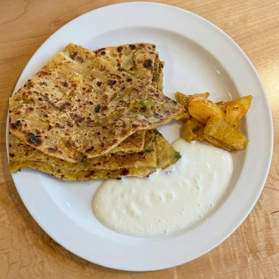A plate of golden-brown paratha, mango pickle, and a dollop of white yogurt on a wooden table.