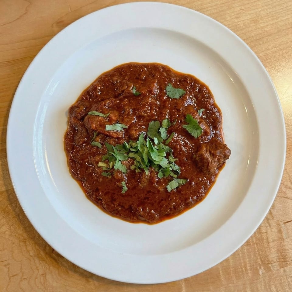 A rich, dark red curry dish, garnished with fresh green cilantro, served on a white plate.